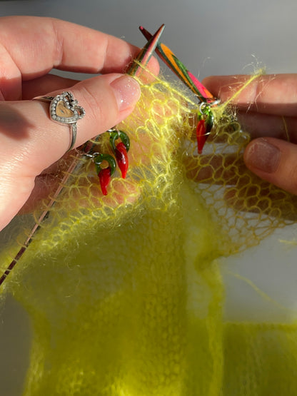 3 ring stitch markers for knitting with small glass lampwork chilies hanging from them being used on a neon green mohair knitted piece. The chilies are mainly red with a green top.The stitch markers are placed on the knitting needles between stitches.