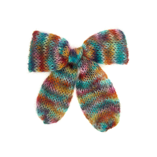 A bright rainbow knitted mohair bow on a white background. The colours fall in vague stripes, although look more splotchy than stripey.