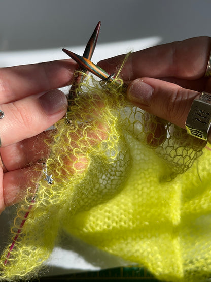 Neon green mohair knit panel on needles with 5 ring stitch markers with star charms between the stitches