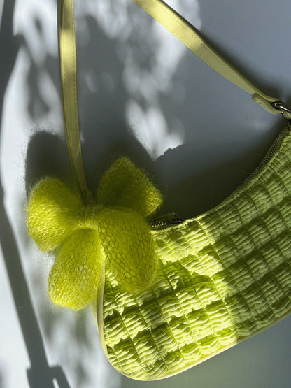 A bright, neon green knitted mohair bow laying on a small, bright green ruched shoulder handbag