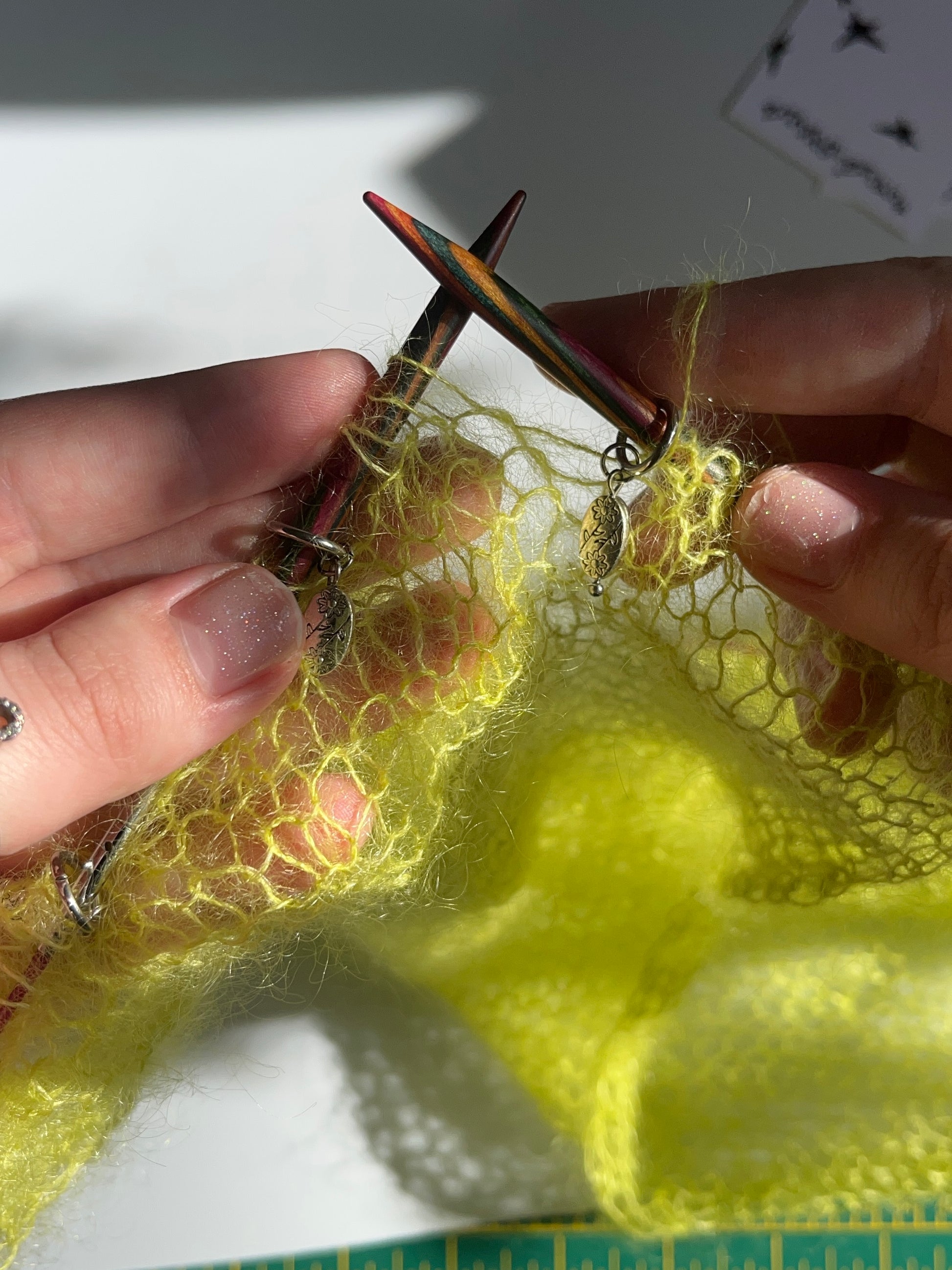 Vintage florals knitting stitch markers being used on a neon green knitted mohair piece. The stitch markers are sitting on the knitting needles between stitches