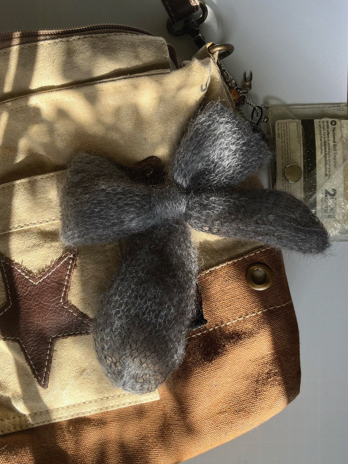 A mid-to-dark grey knitted mohair bow laying on an ivory and brown canvas crossbody bag