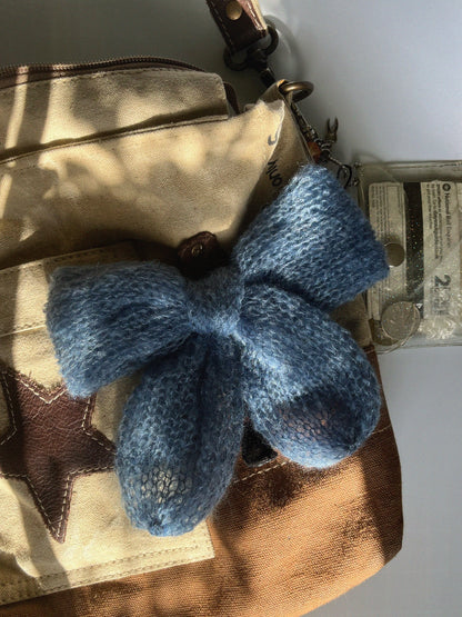 A cornflower-blue knitted mohair bow laying on an ivory and brown canvas crossbody bag