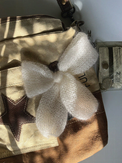 A white knitted mohair bow laying on an ivory and brown canvas crossbody bag